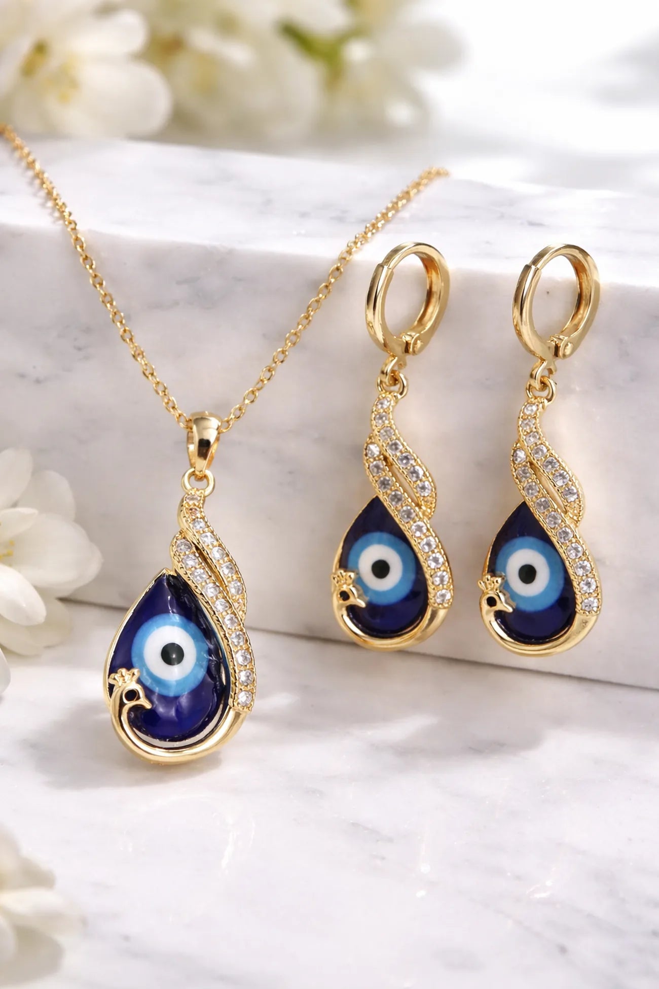 Gold jewelry set with blue eye design on a white marble surface with flowers