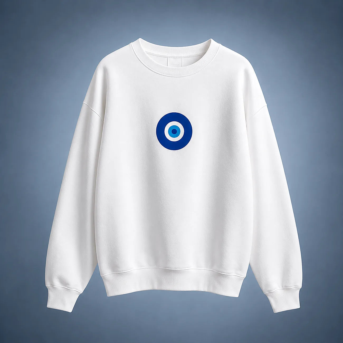 A white crewneck sweatshirt featuring a blue and white circular evil eye graphic on the center chest, displayed against a blue-gray gradient background.