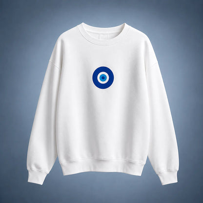 A white crewneck sweatshirt featuring a blue and white circular evil eye graphic on the center chest, displayed against a blue-gray gradient background.