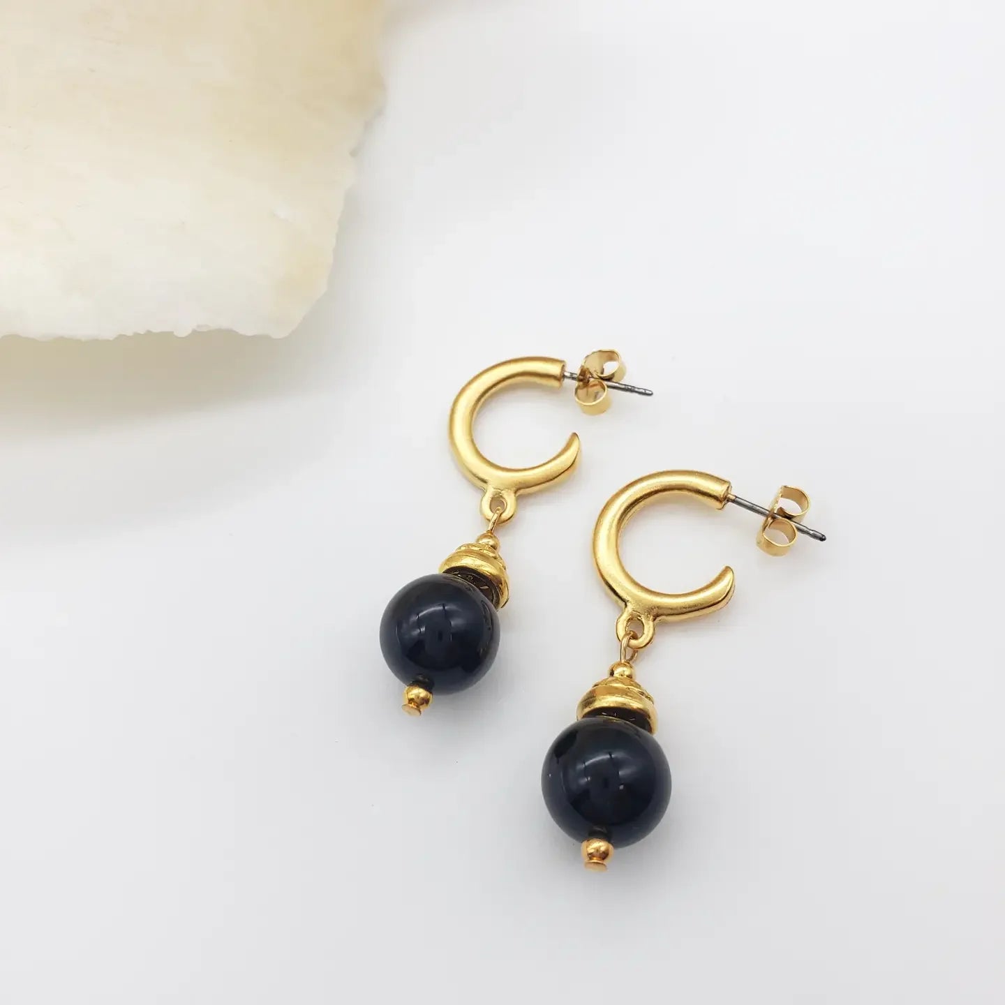 Gold hoop earrings with black beads on a light background