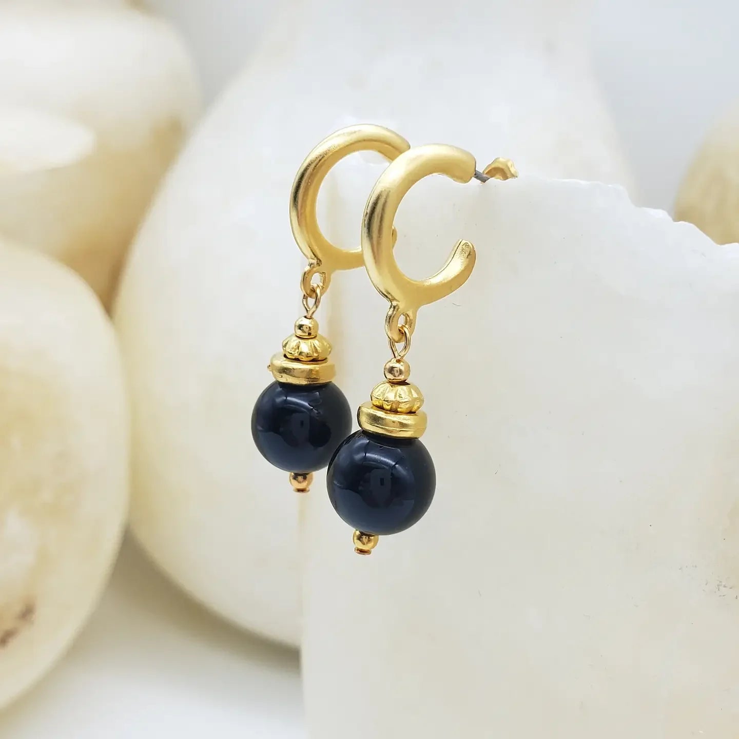 Gold earrings with black onyx beads on a white shell background