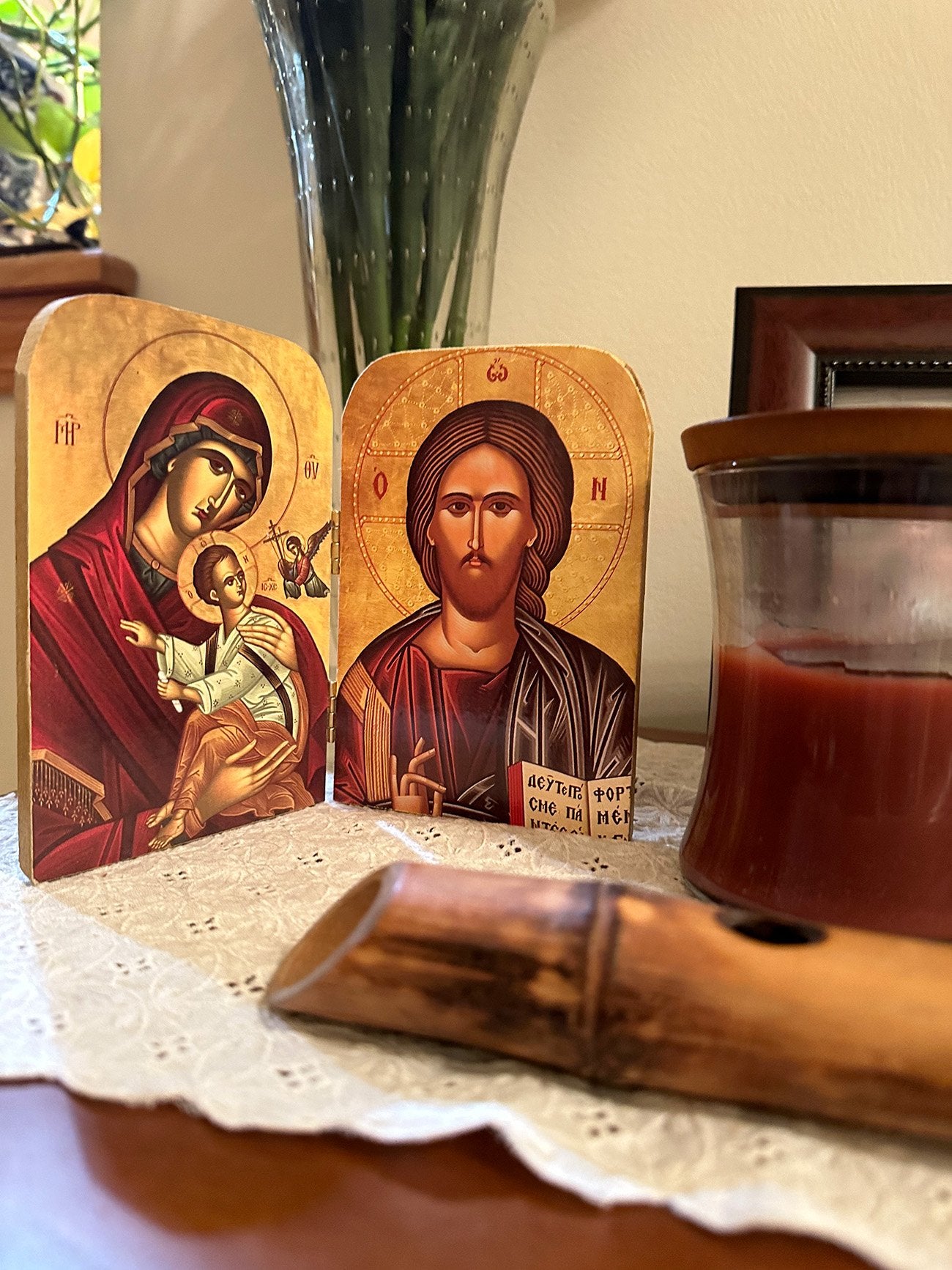 Religious icon diptych of the Virgin Mary and Jesus Christ on a table with a candle and vase in the background