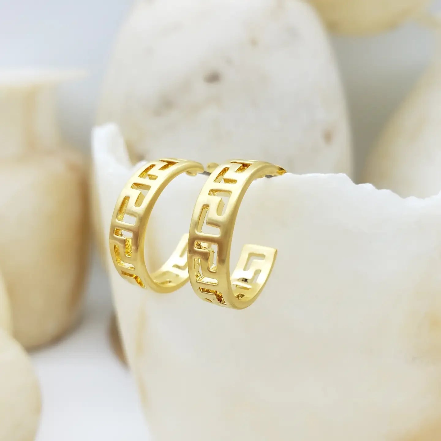 Gold Greek key hoop earrings on a white surface with a neutral background