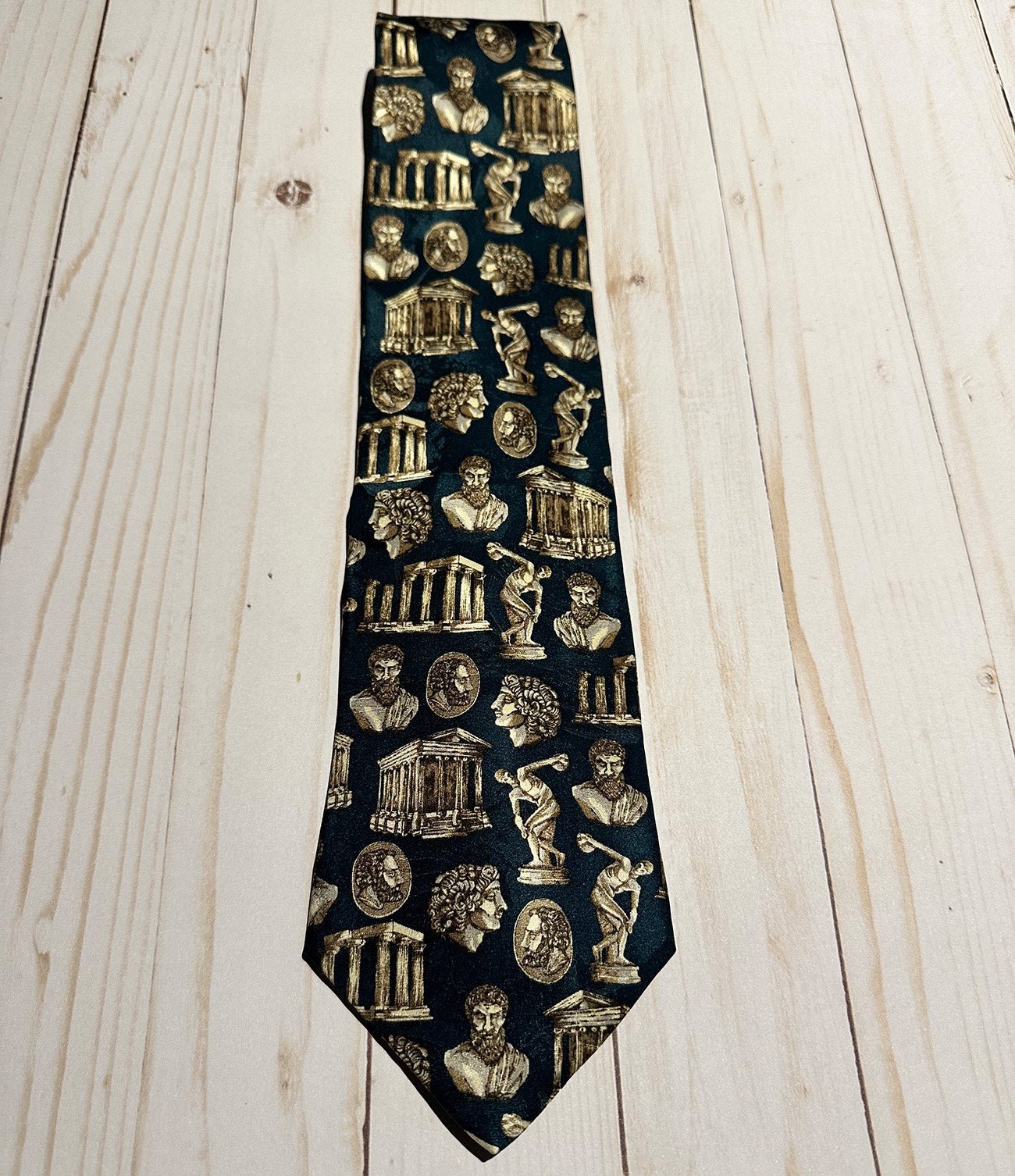 Teal tie with gold architectural and classical Greek figures pattern on a wooden surface