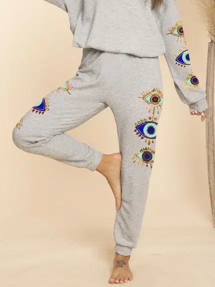 Gray sweatshirt and pants with evil eye designs on a beige background