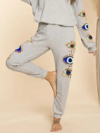 Gray sweatshirt and pants with evil eye designs on a beige background