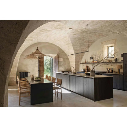 A modern kitchen and dining area set within a rustic stone building featuring arched ceilings, a dark wood island, a dining table with wooden chairs, and pendant lighting.