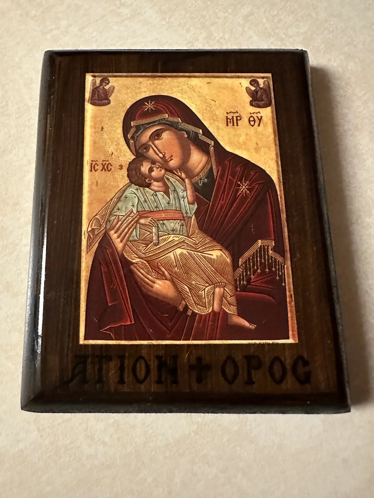 Icon of a religious figure holding a child in a wooden frame on a beige background