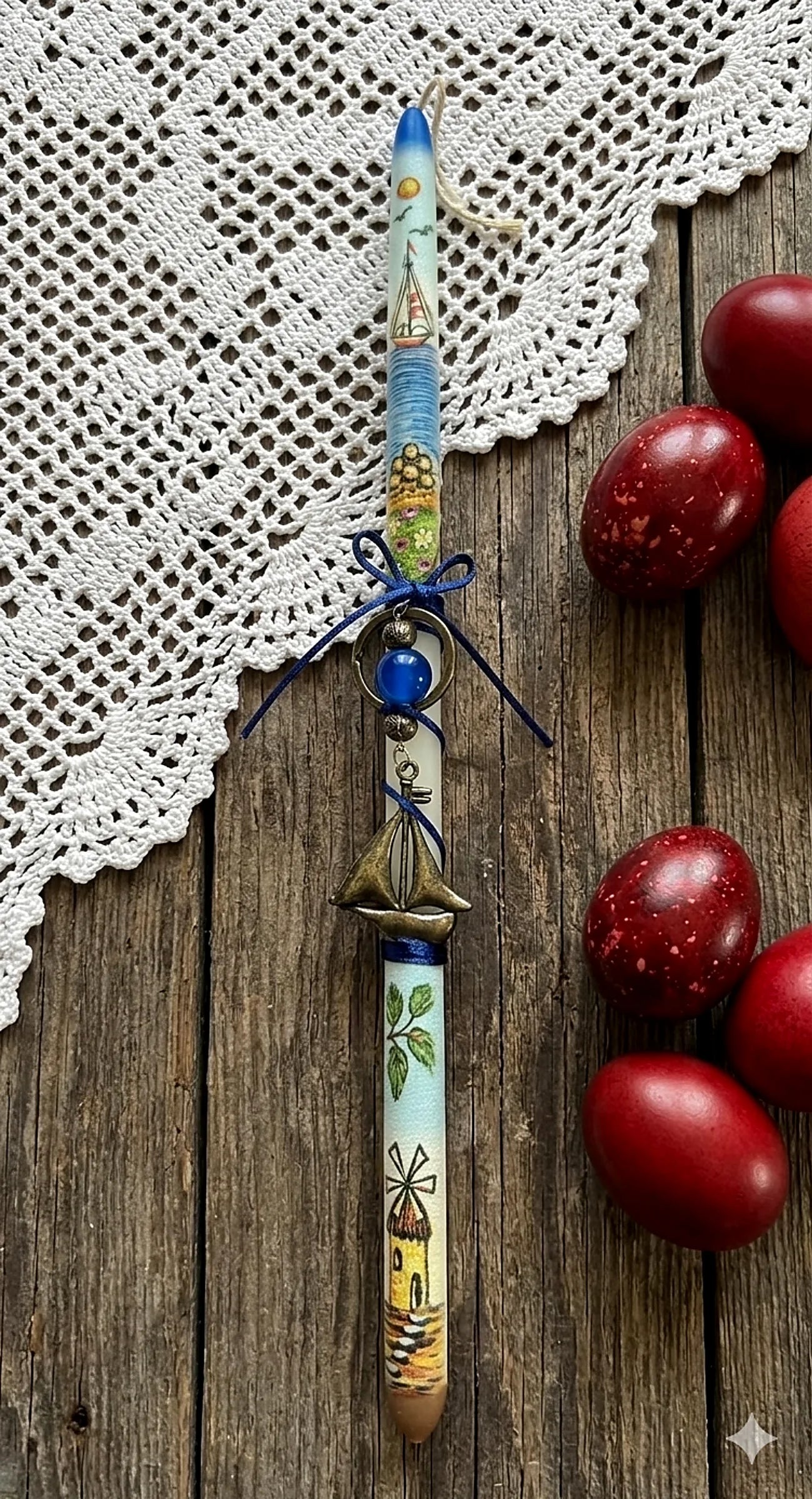 Greek Orthodox Easter candle with artistic design on a wooden surface with red egs and lace fabric.