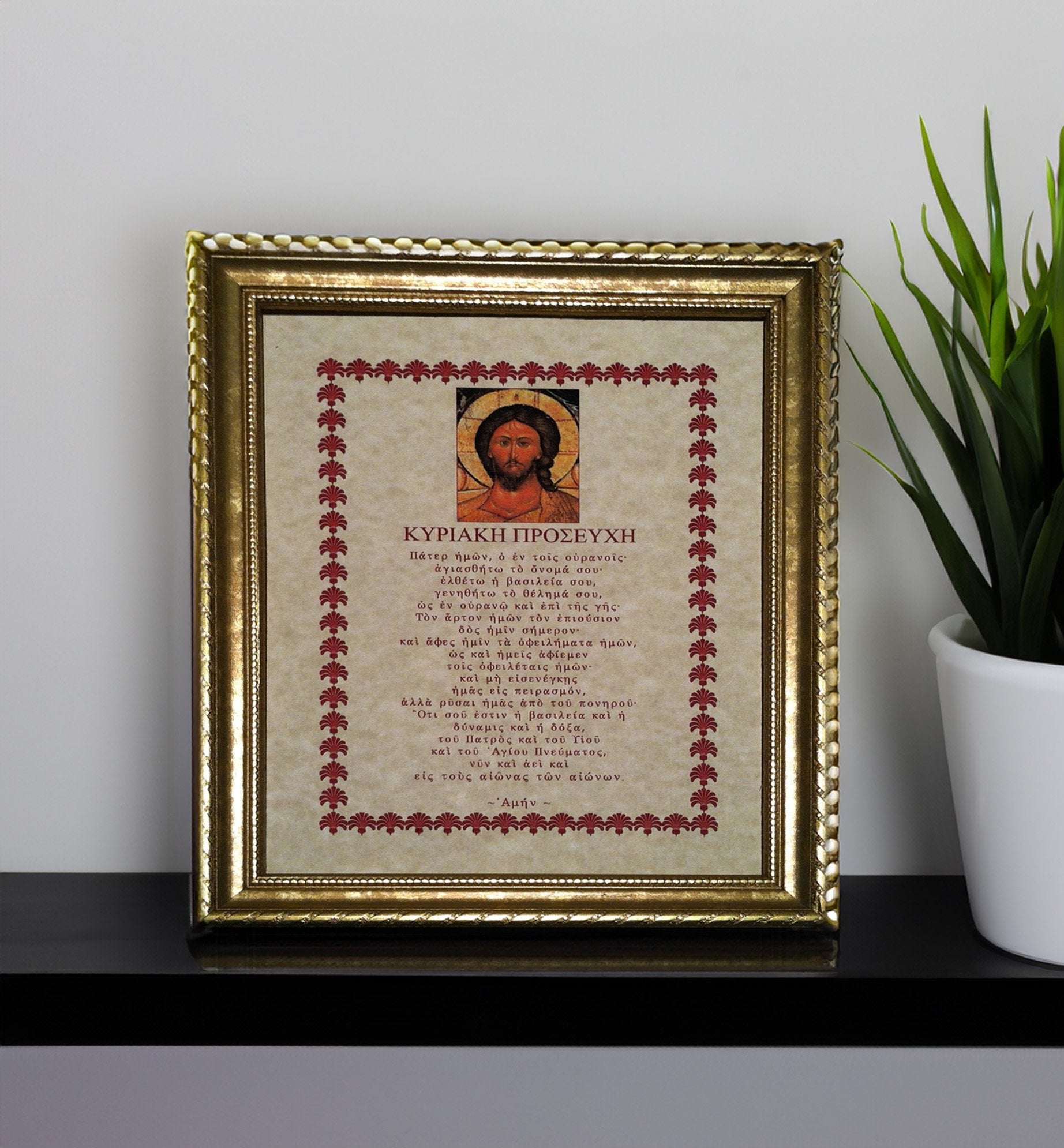 Framed artwork with religious Greek text and icon on a shelf with a plant