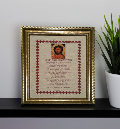 Framed artwork with religious Greek text and icon on a shelf with a plant