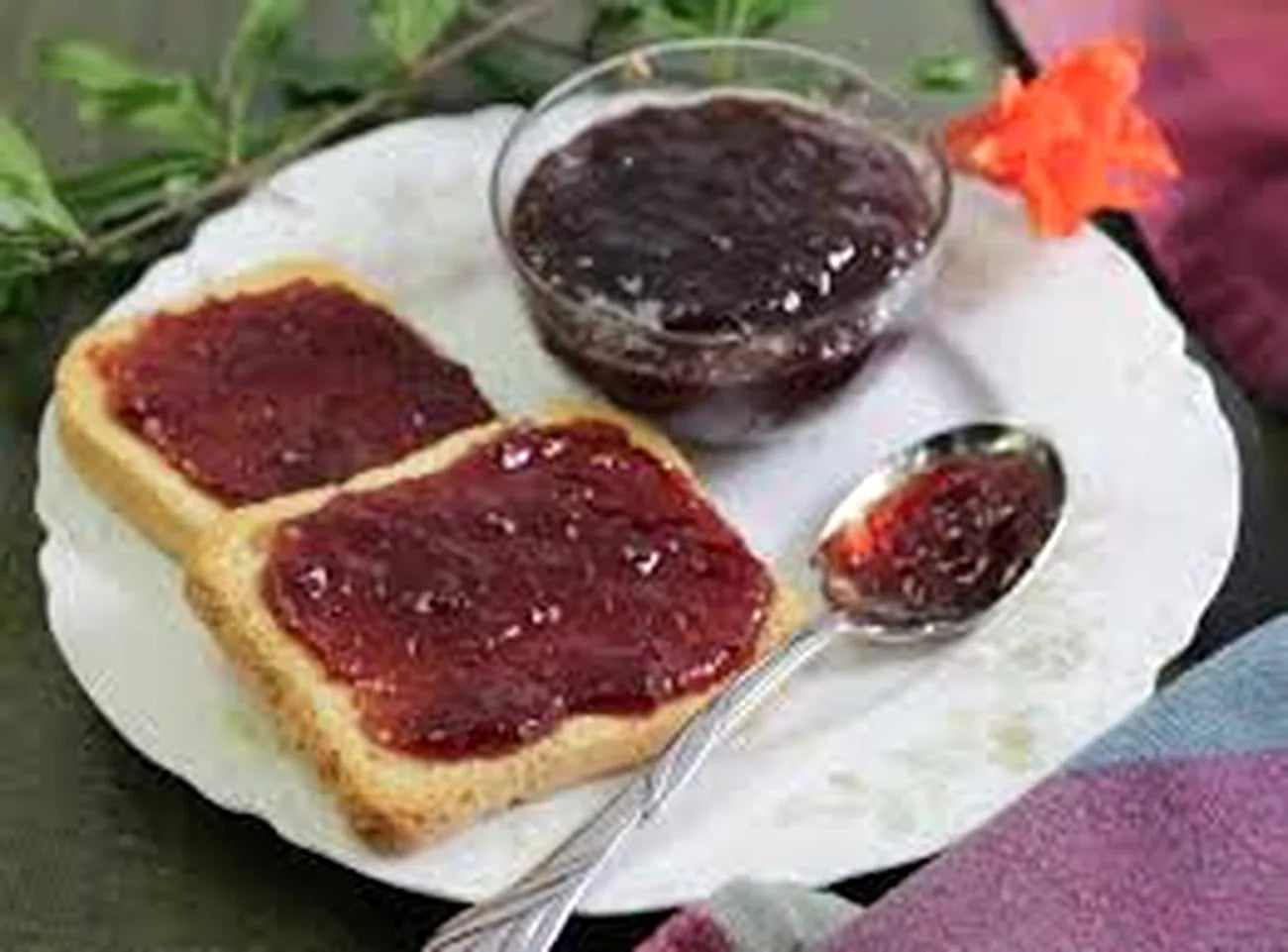 Toast with jam on a plate with a bowl of jam and a spoon.