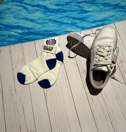 Socks with 'Proud to be Greek' and blue coat of arms accents on a wooden deck by a pool