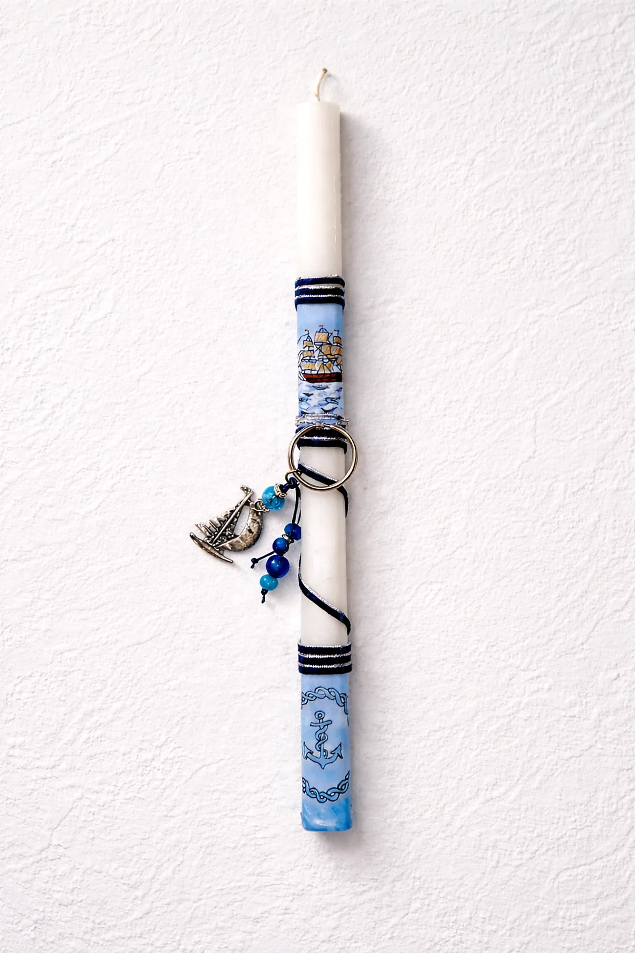 Decorative candle with blue and white pattern and charms on a textured white background