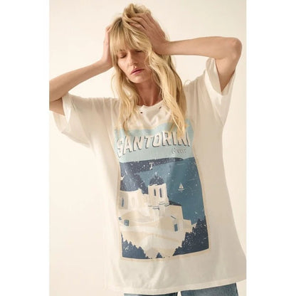 Woman wearing a distressed graphic tee with "Santorini Greece" and scenes of the domed churches and see on a beige background